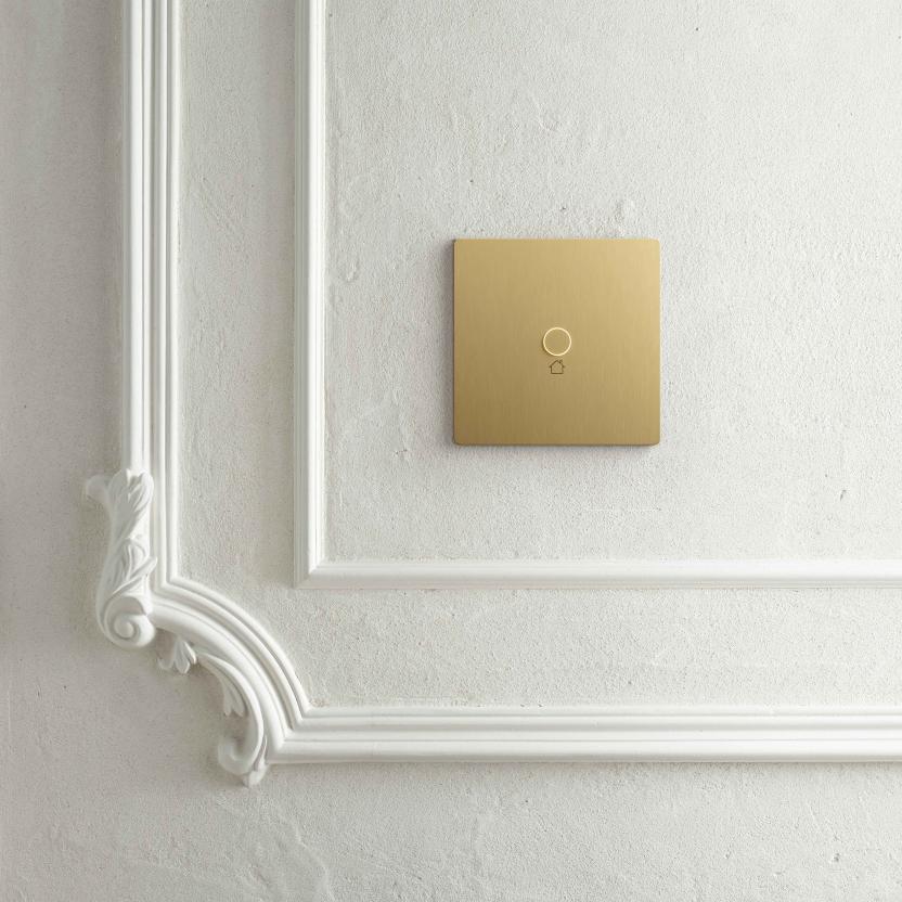 Brushed brass Lutron keypad mounted on a white ornate plaster wall.