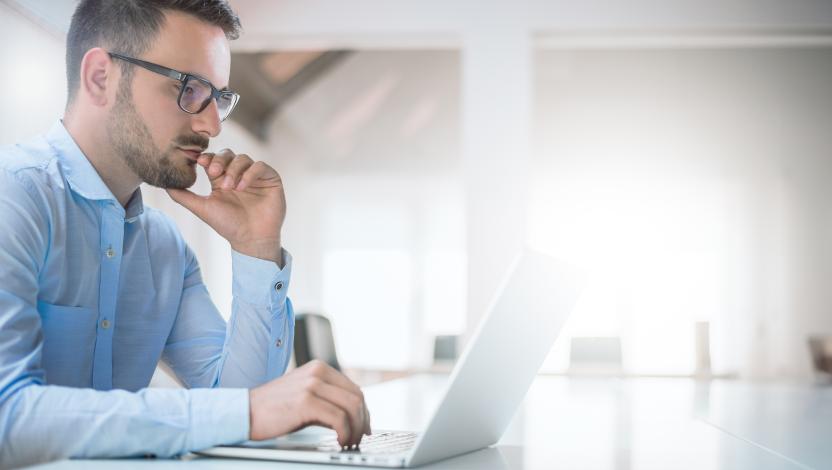 Man with glasses and beard sits at an open laptop.