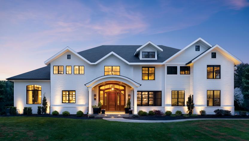 Multi-level mansion at sunset, each room well-lit with matched interior lighting.