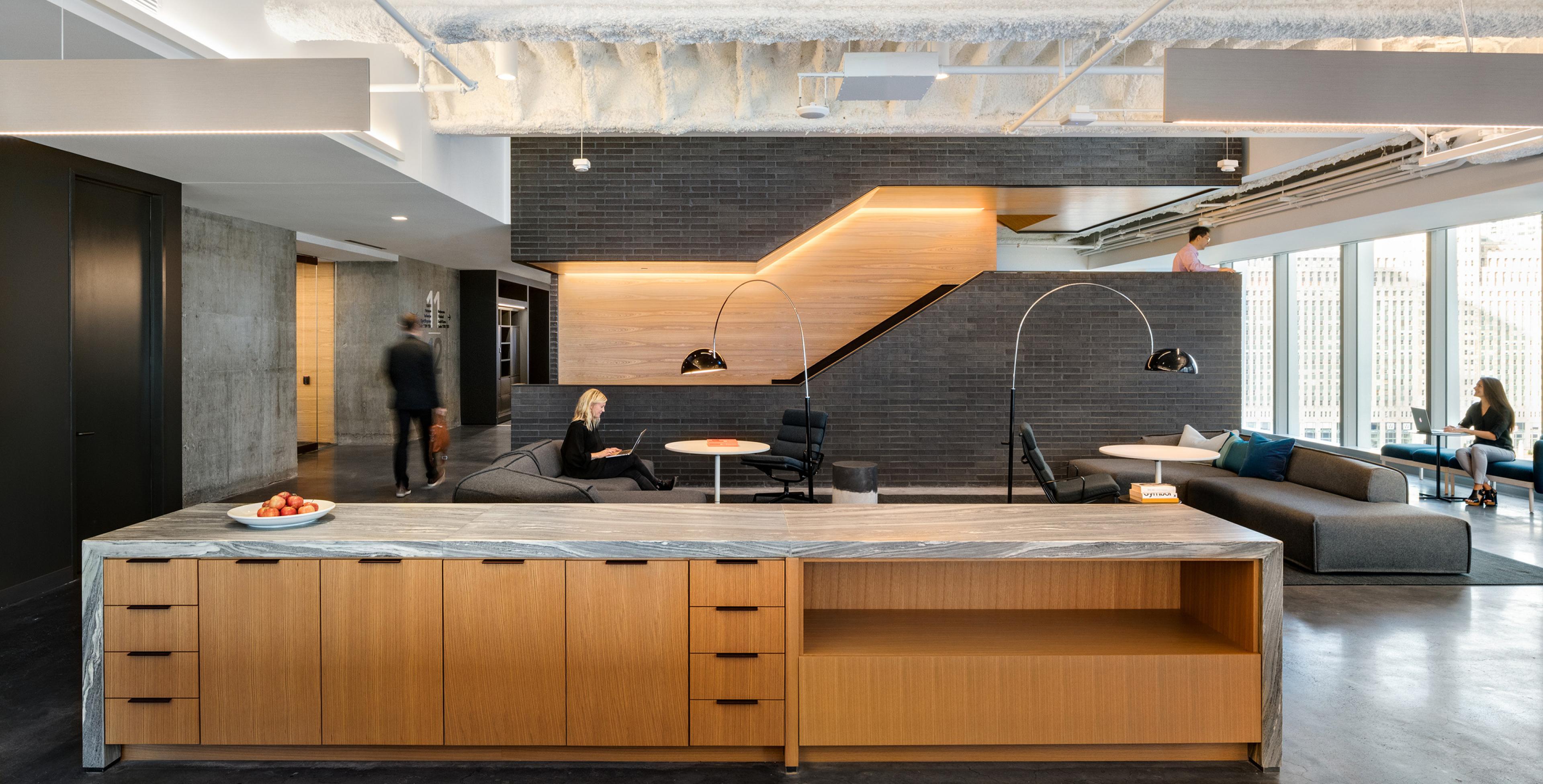 Central circulating stair at a modern office combines grey brick and oak wood surfaces with tape lights integrated into the paneling.