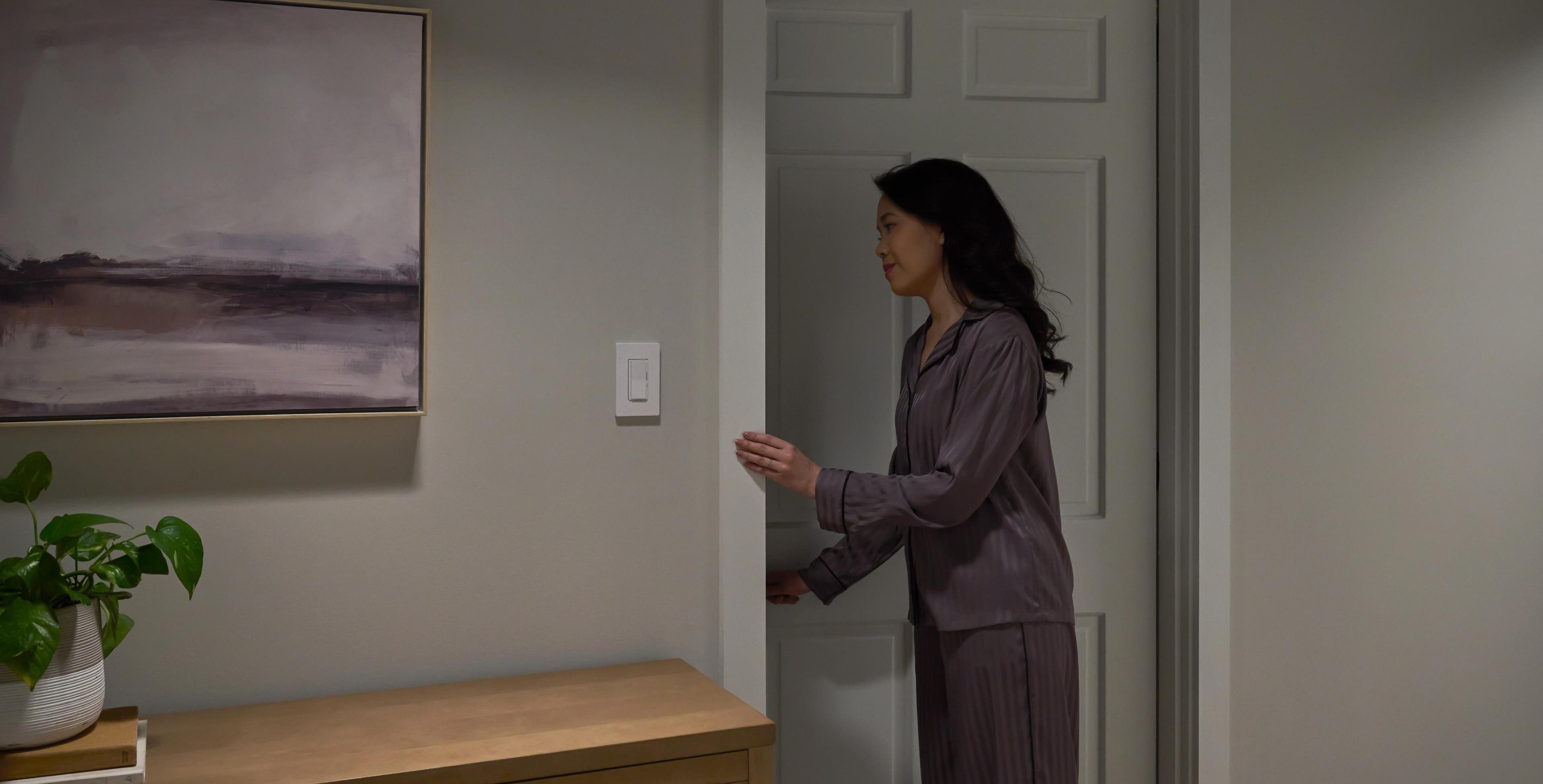 A woman closes a bedroom door at night, while the hallway is perfectly dimmed by the dimmer switch on the wall.
