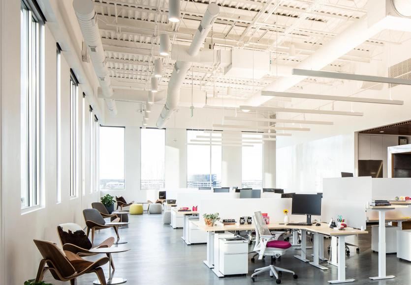 Modern open office with city views lit by in-fixture linear luminaire smart lighting.
