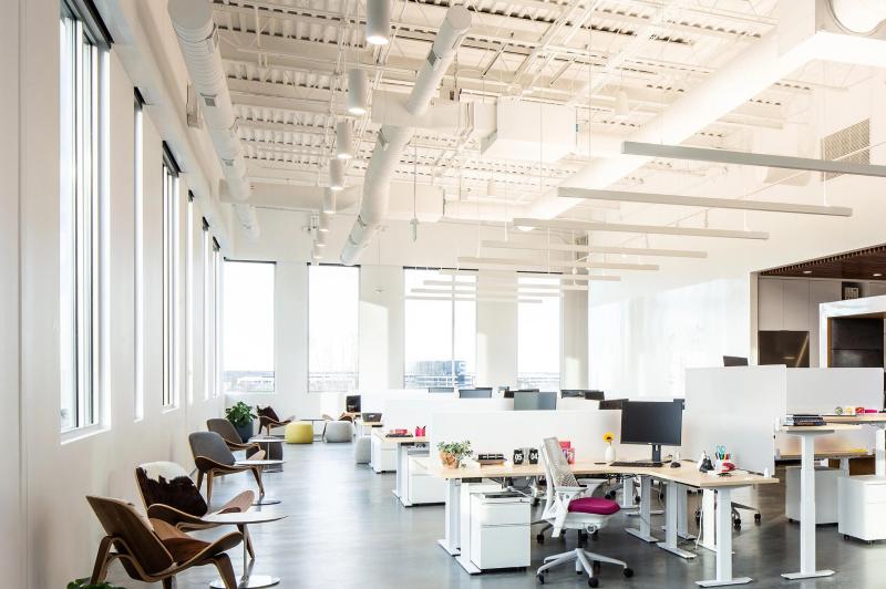 Modern open office with city views lit by in-fixture linear luminaire smart lighting.