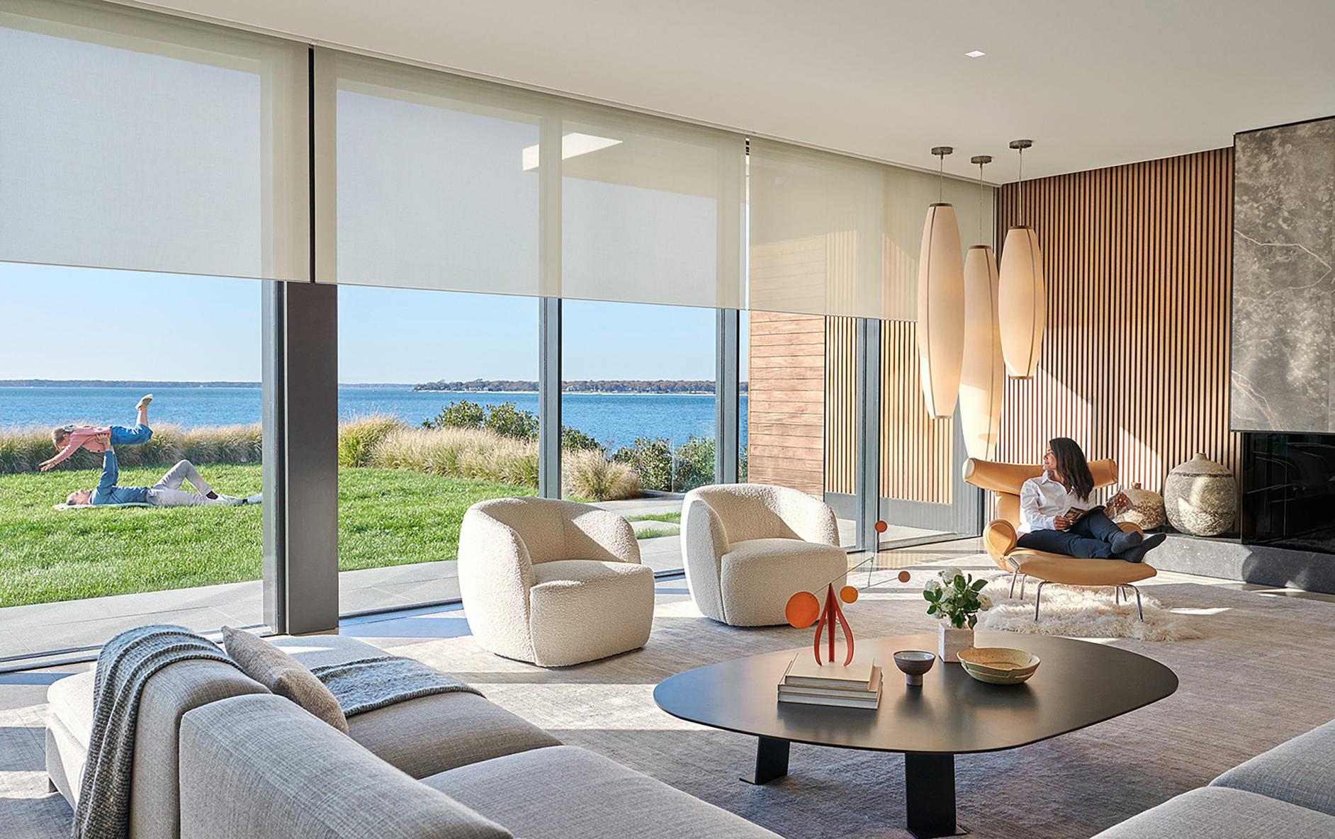 Modern living room with automated shades,  floor-to-ceiling windows, and a waterfront view.